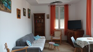 A living room with a grey sofa, a wooden cabinet, a television, and a dining table with chairs. - 3min walk BEACHES, PARKING Town Hall, Pedestrian street Quiet 42 m2 CLIM 3p max (Menton)