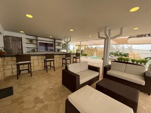 Un espace extérieur aménagé en terrasse, avec des meubles en osier, un bar et une piscine.