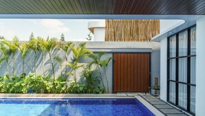 A modern outdoor pool area with a clear blue pool, surrounded by tropical plants and a wooden door. - Sunshine City View Villa 6BR wth a private Heated Pool (Cimenyan)