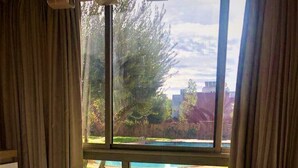 A dining area with a table and chairs, a window with curtains, and a view of a grassy yard and trees. - Luxurious modern apartment Coralia Marrakech for rent (Marrakech)