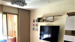 A modern living room with a flat-screen TV, a sofa, a coffee table, and a dining area. - Luxurious modern apartment Coralia Marrakech for rent (Marrakech)