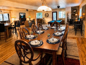 A dining room with a long wooden table set for a meal, surrounded by chairs.