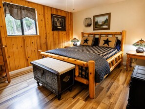 A wooden-paneled room with a bed, a bench, a lamp, and artwork on the walls.