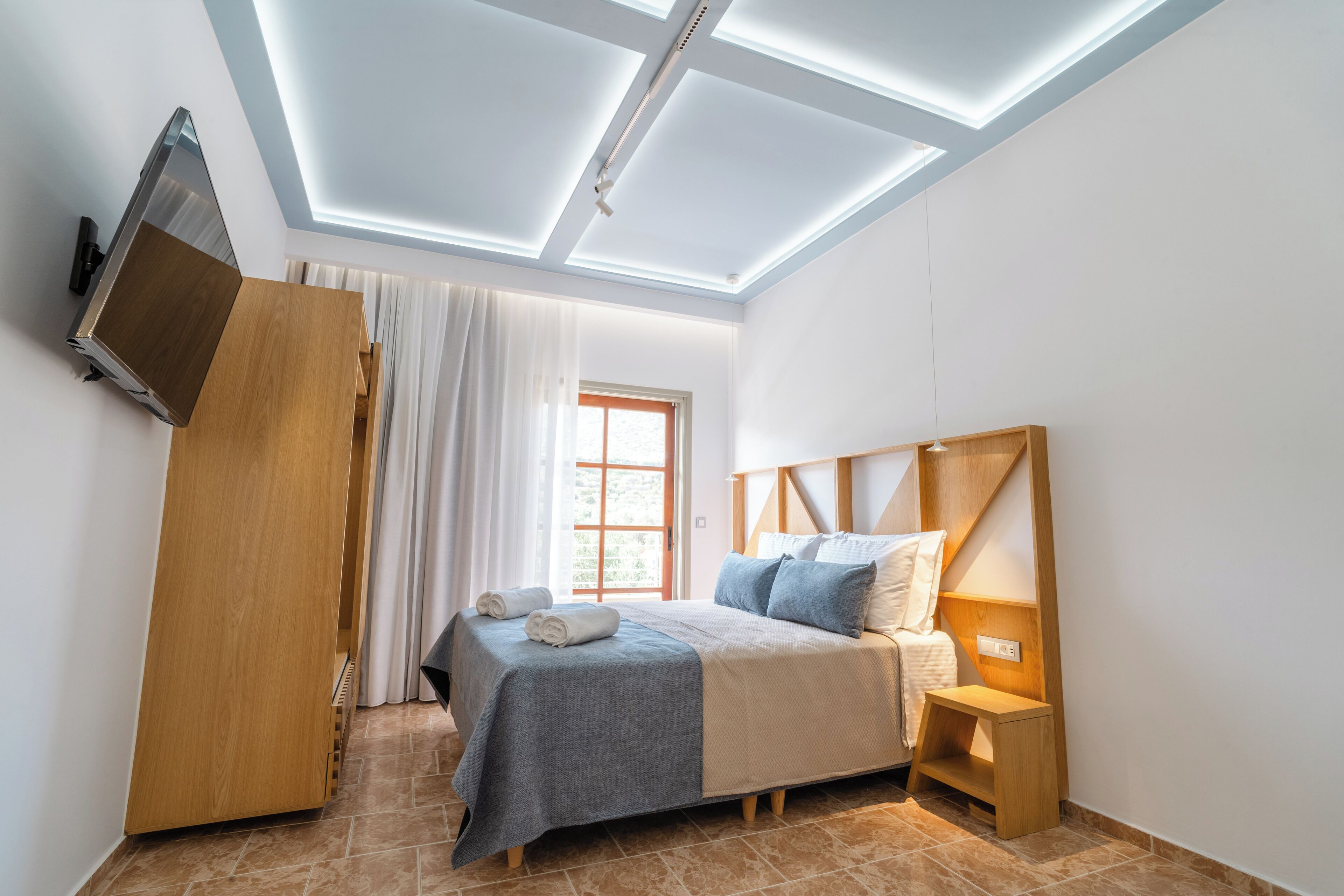 A modern bedroom with a skylight, a bed with a wooden headboard, a nightstand, and a TV mounted on the wall.