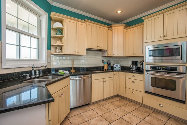 A kitchen with beige cabinets, a black countertop, a stainless steel dishwasher, a microwave, and an oven.