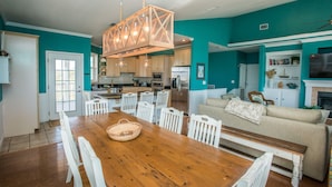 A spacious kitchen with modern appliances, a dining area with a wooden table and white chairs, and a living room with a beige sofa and a fireplace. - Sea Grass Neighborhood * Private Pool 5 Bdrms (Cape San Blas)