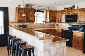 A kitchen with wooden cabinets, a granite countertop, a built-in stove, and a bar area with stools.