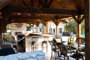 An outdoor kitchen area with a stone wall, wooden beams, and bar stools. - Pura Vida Private Pool, Wi-Fi, @ Frio River Vacation Rentals (Concan)