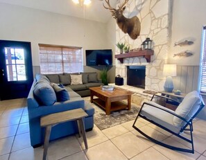 A living room with a stone fireplace, a mounted deer head, a television, and a blue sofa.