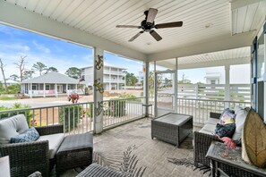 A covered outdoor area with wicker furniture, a ceiling fan, and a view of a residential area.