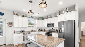 A modern kitchen with white cabinets, granite countertops, stainless steel appliances, and a central island with bar stools. - (4 Minute Walk to Beach) Screened in porch & MBR  on ground level (Cape San Blas)