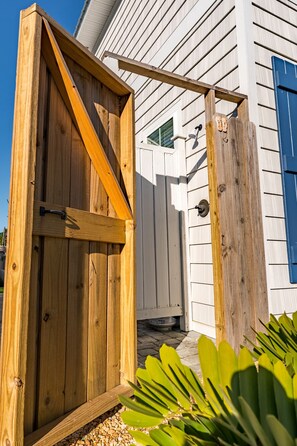 A wooden gate leading to a house with white siding and a blue door.