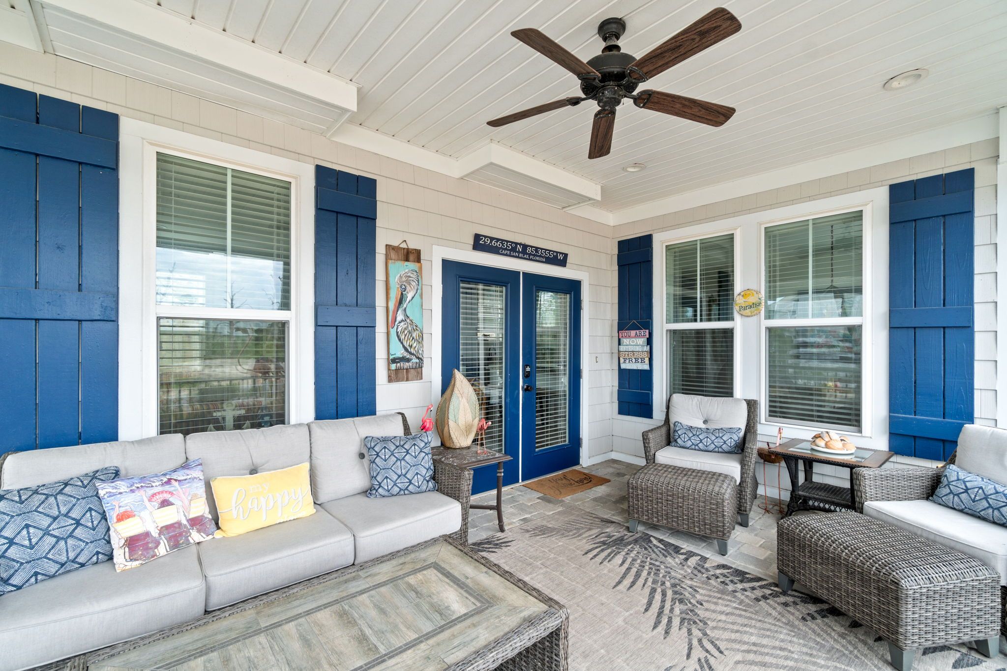 A covered porch with a ceiling fan, a blue door, and a seating area with a sofa and chairs.