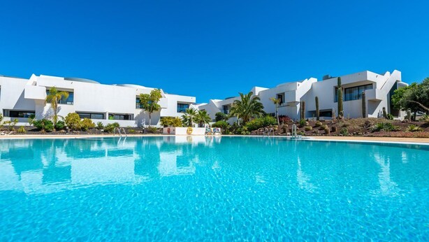 A modern resort with a clear blue pool, white buildings, and tropical landscaping. - Cozy apartment with pool (CN)