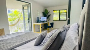A bedroom with a bed, a desk with a computer, and a window with blinds.