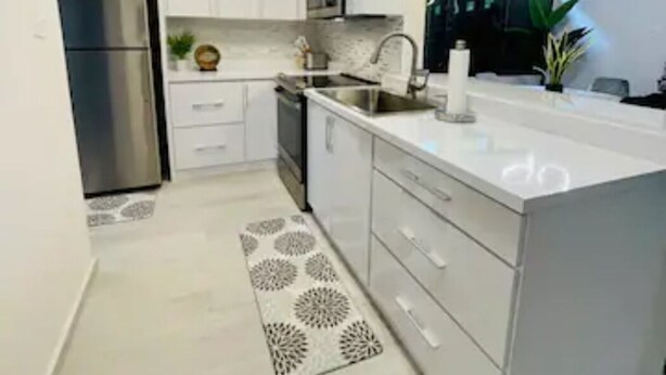 A modern kitchen with white cabinets, stainless steel appliances, and a patterned rug.