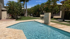A rectangular swimming pool with clear blue water, surrounded by a stone deck and palm trees.
