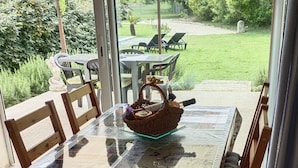 En overdækket terrasse med et bord og stole, en fletkurv og udsigt til en græsplæde.