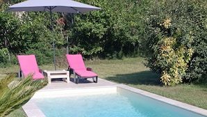 Et rektangulært swimmingpool med flisekant, omgivet af græs og palmer.