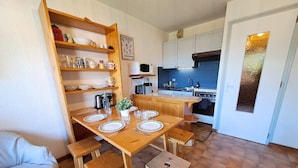 A compact kitchen with a dining table set for four, wooden cabinets, a microwave, and a stove. - Studio at the foot of the ice rink (Le Grand-Bornand)