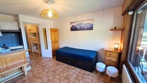 A compact room with a bed, a small table, a bench, a desk, and a window. - Studio at the foot of the ice rink (Le Grand-Bornand)