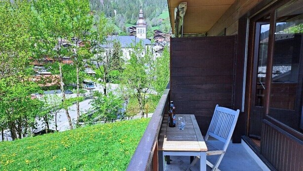 A balcony with a table and chair, overlooking a green area and a distant building. - Studio at the foot of the ice rink (Le Grand-Bornand)