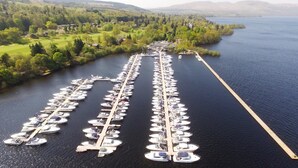 An aerial view of a marina with numerous boats docked in a structured layout, surrounded by lush greenery and hills in the background. - Romantic / Valentines Lodge by Loch Lomond (Alexandria)