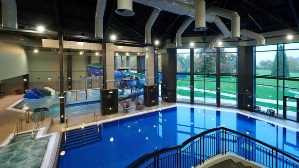 An indoor swimming pool with a water slide, seating area, and large windows offering a view of the outdoors. - Romantic / Valentines Lodge by Loch Lomond (Alexandria)