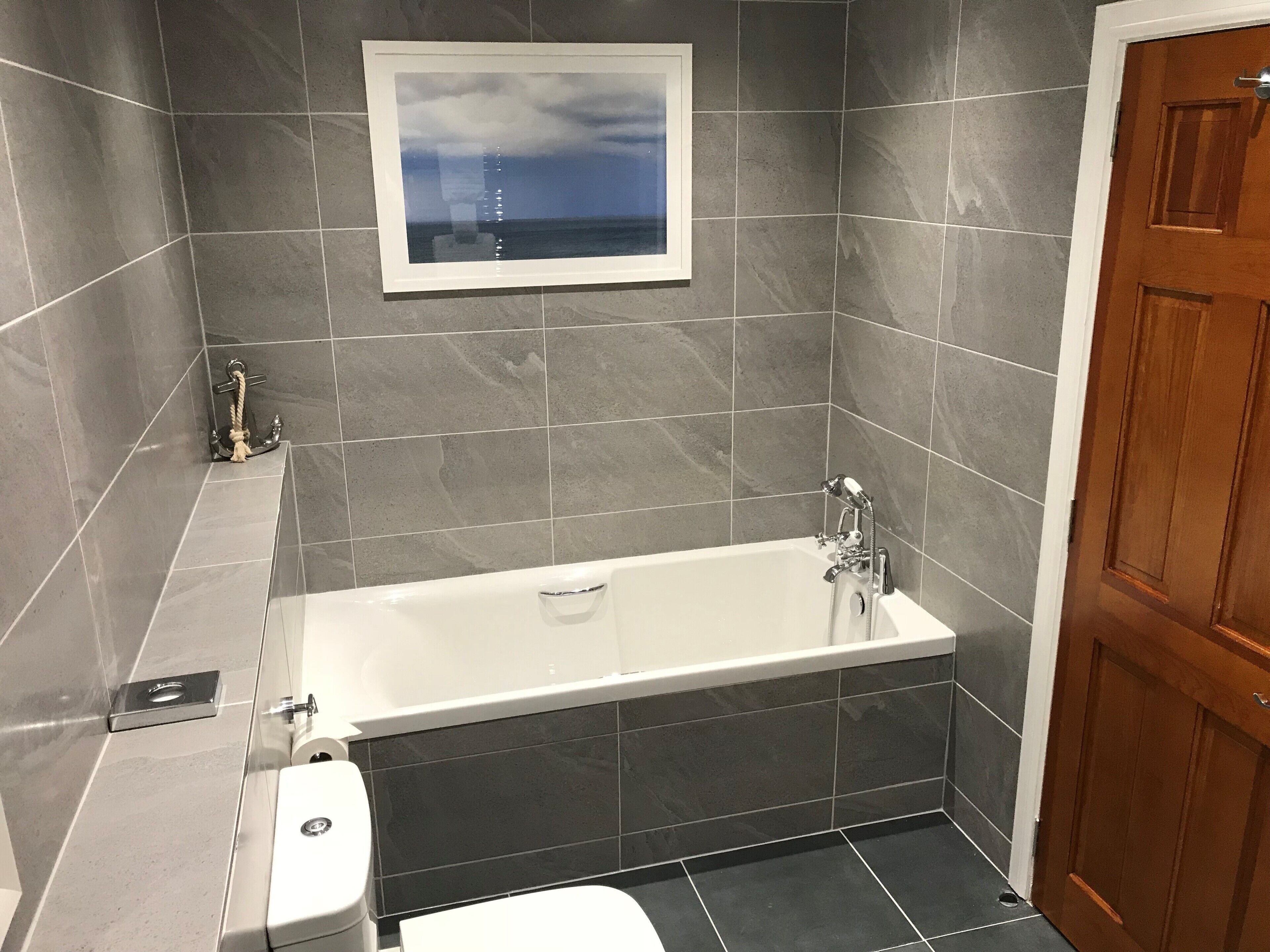 A bathroom with a bathtub, toilet, and a framed picture on the wall.