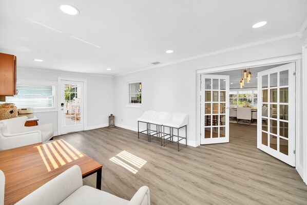 Una habitación amplia con suelo de madera, paredes blancas y un comedor con mesa y sillas.