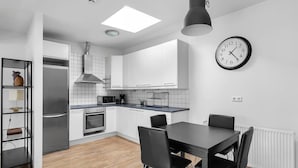 Une cuisine moderne avec des meubles blancs, une table à manger noire et une horloge au mur.