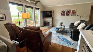 A living room with a fireplace, leather chairs, a glass coffee table, and a large TV. - Large Home on Bull Shoals Lake with Core Lake Access (Midway)