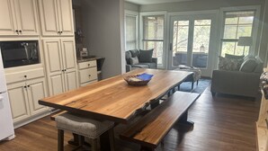 A spacious kitchen with a large wooden table and benches, white cabinetry, and a view of the outdoors through large windows. - Large Home on Bull Shoals Lake with Core Lake Access (Midway)