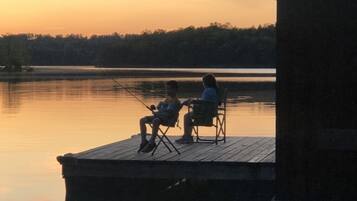 Two people sitting on chairs on a wooden dock by a calm lake during sunset.