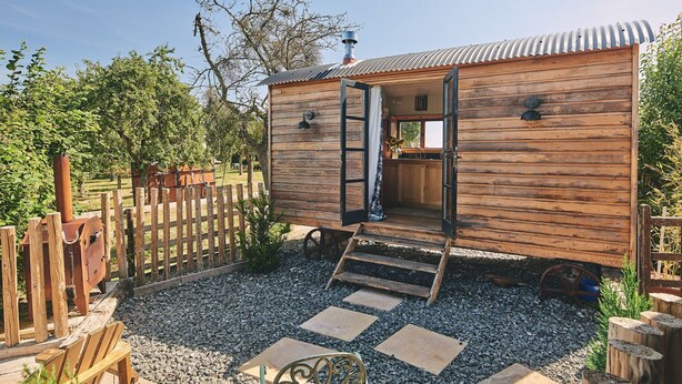 Una cabaña de madera con una zona de cocina, una terraza de madera y un camino de grava.