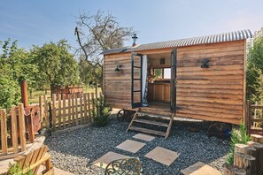 A wooden cabin with a kitchen area, a wooden deck, and a gravel pathway.