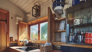 Una cocina con armarios de madera, un lavamanos empotrado, una ventana con vistas a árboles y un estante con utensilios de cocina.