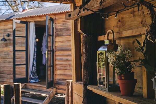 A wooden cabin with an open door, a lantern on the porch, and a potted plant.
