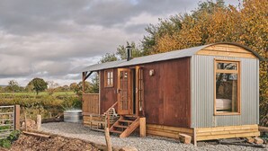 A rustic wooden cabin with a metal roof, a wooden porch, and a small staircase leading to the entrance.