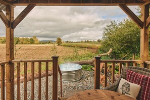 A wooden deck with a metal hot tub, wicker furniture, and a view of a field and trees. - Big Sky Hideaway - Luxury Cottages (Leominster)