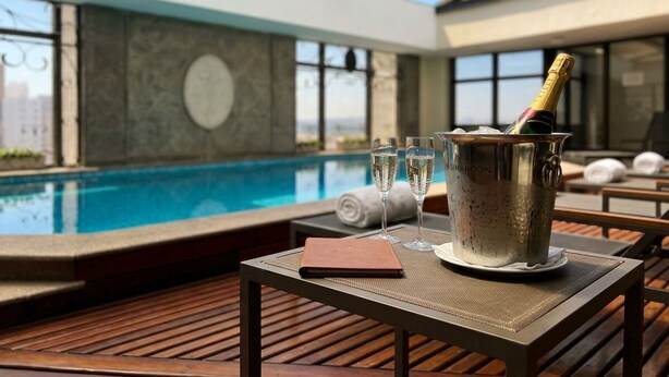 Uma área na beira da piscina com mesa, uma garrafa de champanhe e um caderno.