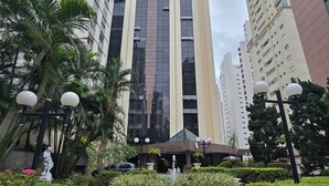 Um edifício moderno com fachada de vidro central, rodeado por vegetação exuberante e uma pequena fonte.