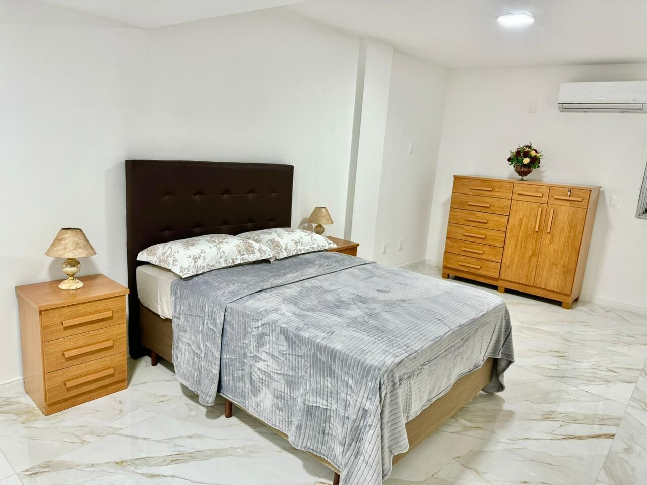 Une chambre à coucher avec un lit, des tables de chevet, une armoire en bois et un sol en marbre.