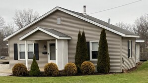 A single-story house with a gabled roof, a front porch, and a small front yard with trimmed bushes and a lawn.