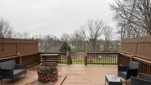 A wooden deck with outdoor furniture, a fire pit, and a view of a house in the background.