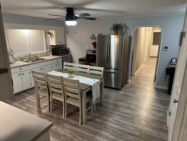 A compact kitchen with a dining area, a ceiling fan, and a refrigerator.