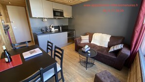 A modern kitchen with grey cabinets, a microwave, and a toaster. There is a dining table with chairs, a brown leather sofa, and a small round table with a candle. - High standing, FOOT OF THE SLOPES and summer activities (Les Menuires)