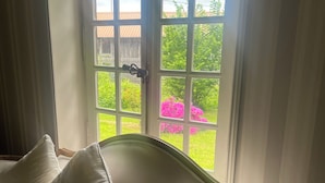 Et værelse med en hvid polstret sofa og et stort vindue med udsigt over en have og et træhegn.