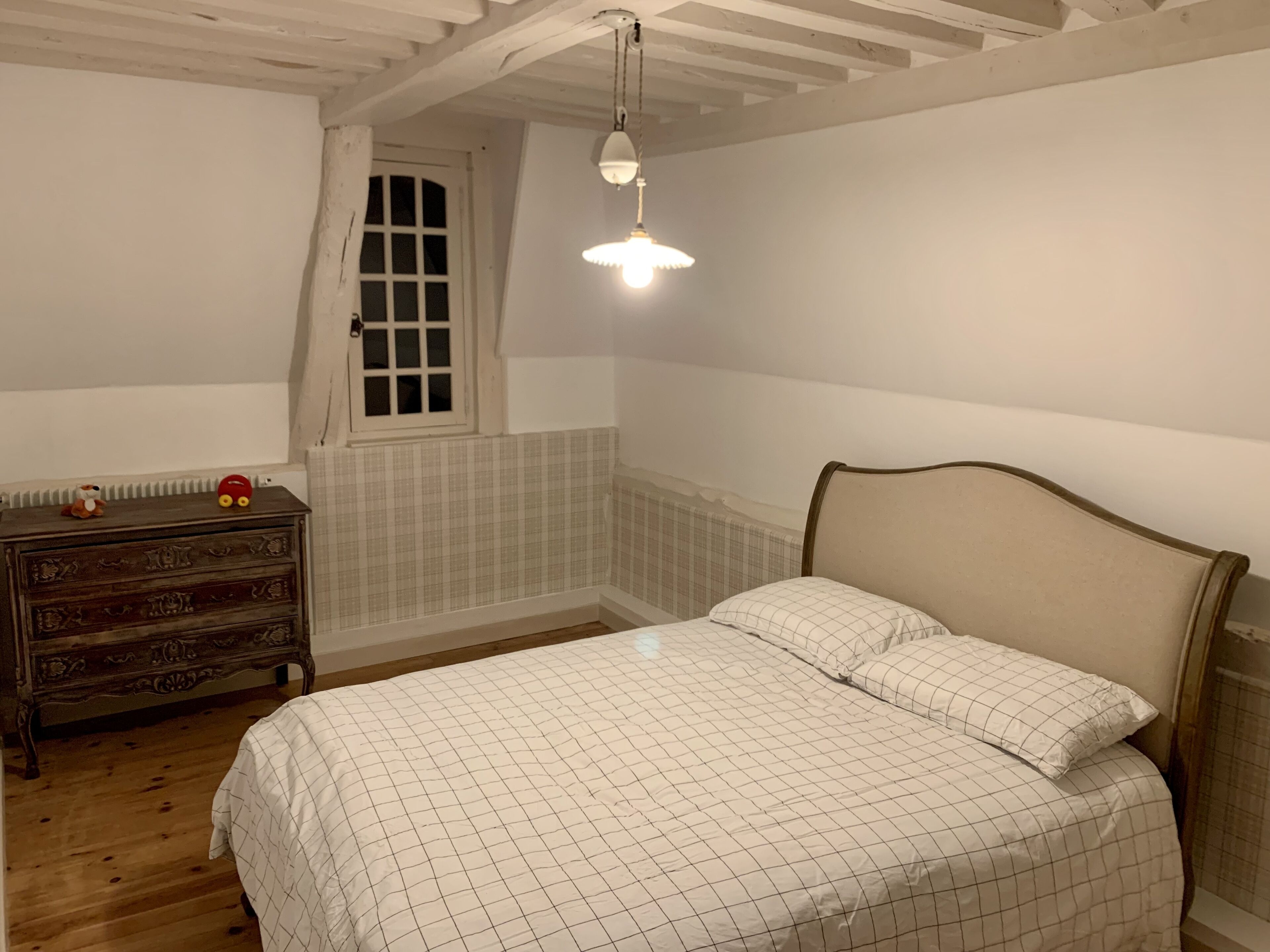 A bedroom with a bed, dresser, and a window with a view.