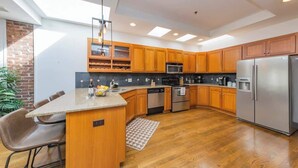A modern kitchen with wooden cabinets, stainless steel appliances, and a built-in island with seating. - 2 Lofts on Broadway Strip - Sleeps 10 (Nashville)